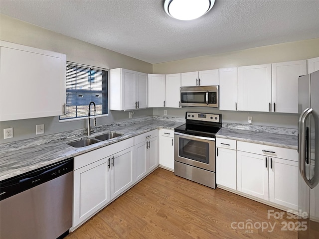 kitchen with stainless steel appliances, a sink, light wood-style flooring, and white cabinets