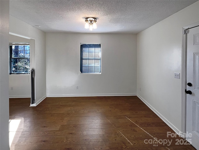 empty room with a textured ceiling, baseboards, and dark wood-style flooring