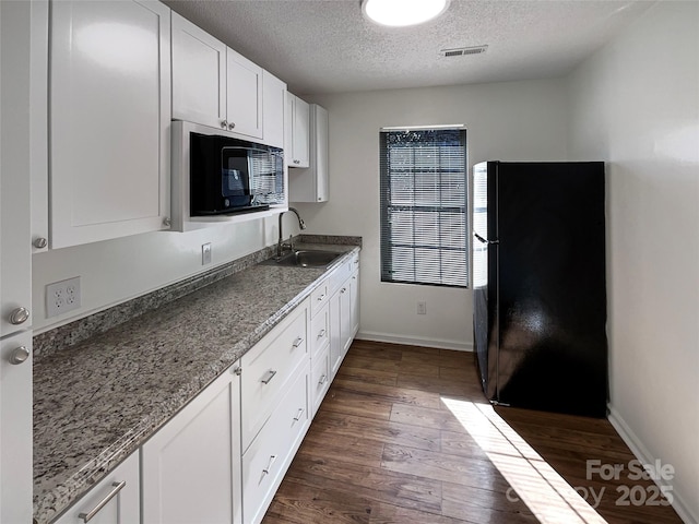 kitchen with dark wood-type flooring, a sink, visible vents, white cabinets, and black appliances