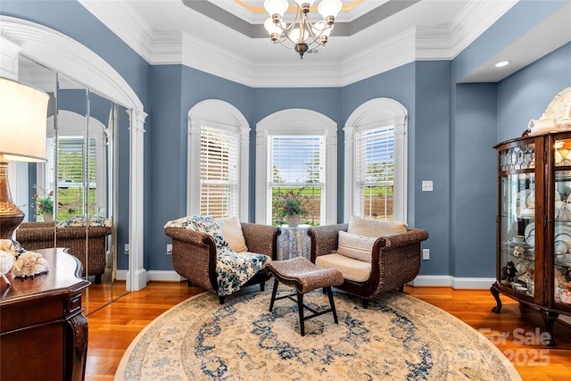 living area with ornamental molding, a notable chandelier, baseboards, and wood finished floors