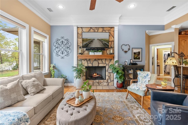 living area featuring recessed lighting, visible vents, light wood-style flooring, ornamental molding, and a stone fireplace