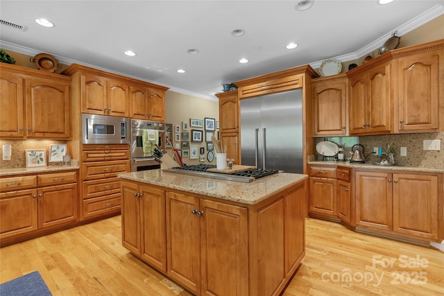 kitchen with built in appliances, light wood-style floors, ornamental molding, brown cabinets, and light stone countertops