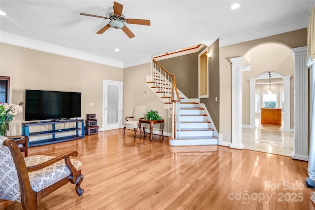 living room featuring arched walkways, a ceiling fan, light wood-type flooring, ornate columns, and crown molding