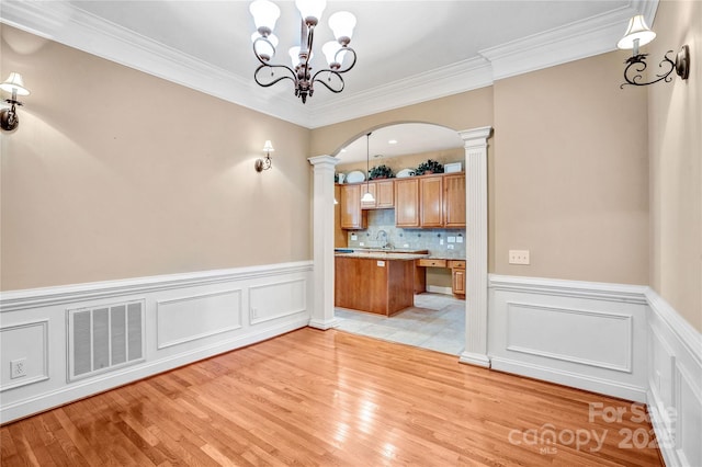 unfurnished dining area featuring arched walkways, a sink, visible vents, light wood finished floors, and decorative columns