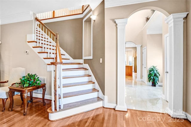 stairs featuring arched walkways, wood finished floors, baseboards, ornate columns, and crown molding