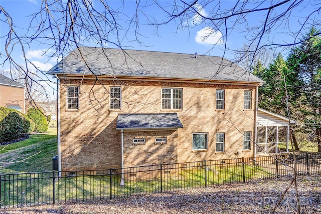 back of house with a sunroom, a fenced backyard, brick siding, and roof with shingles