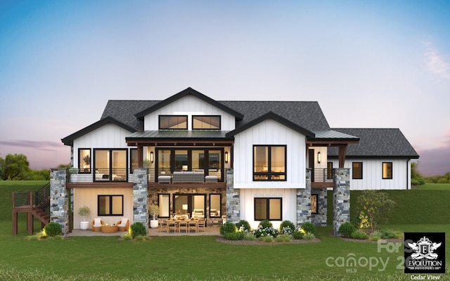 rear view of house with a balcony, stone siding, roof with shingles, a lawn, and a patio area