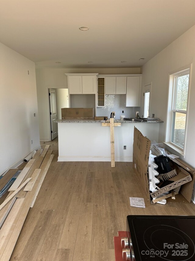 kitchen with tasteful backsplash, glass insert cabinets, white cabinetry, and light wood-type flooring