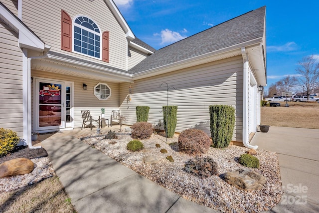 view of exterior entry featuring a shingled roof and an attached garage