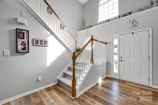 foyer featuring a towering ceiling, baseboards, and wood finished floors