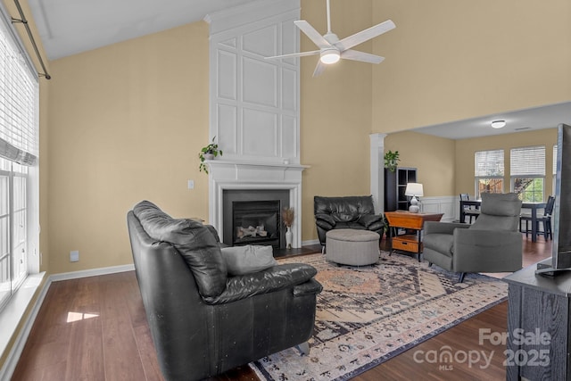 living room with a large fireplace, a high ceiling, wood finished floors, baseboards, and decorative columns