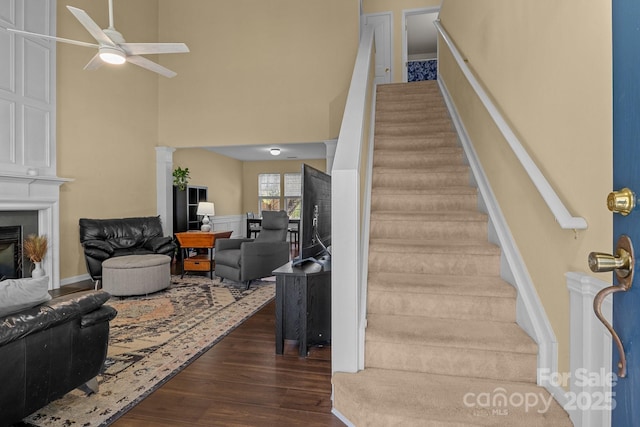 stairway featuring ceiling fan, a high ceiling, a fireplace, wood finished floors, and decorative columns