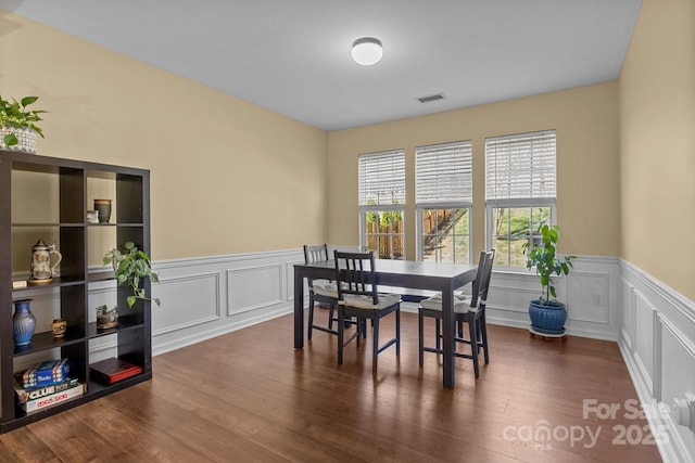 dining space featuring visible vents, a decorative wall, dark wood-style flooring, and wainscoting