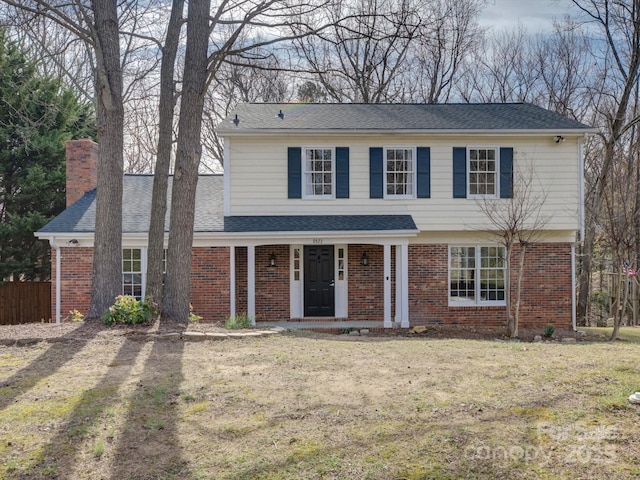 view of front facade featuring a chimney, a porch, roof with shingles, a front lawn, and brick siding