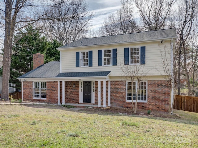 view of front of home with brick siding, a chimney, a shingled roof, fence, and a front lawn