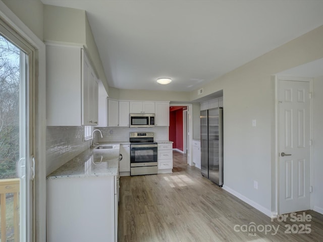 kitchen with baseboards, white cabinets, appliances with stainless steel finishes, light wood-type flooring, and backsplash