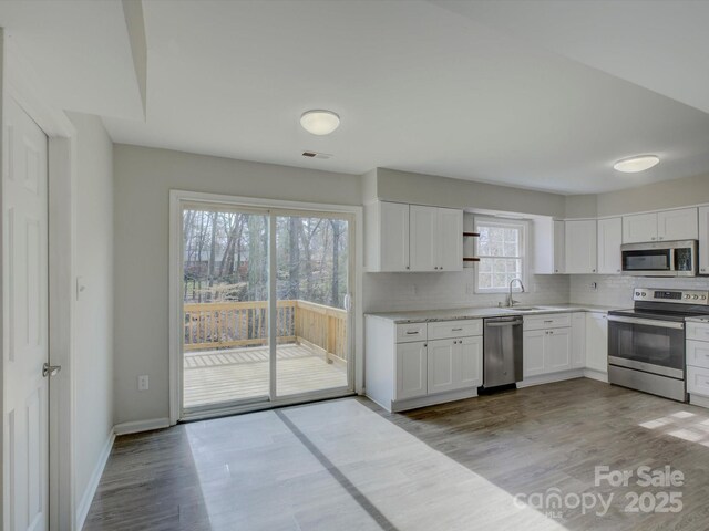 kitchen with stainless steel appliances, white cabinetry, light wood finished floors, and tasteful backsplash