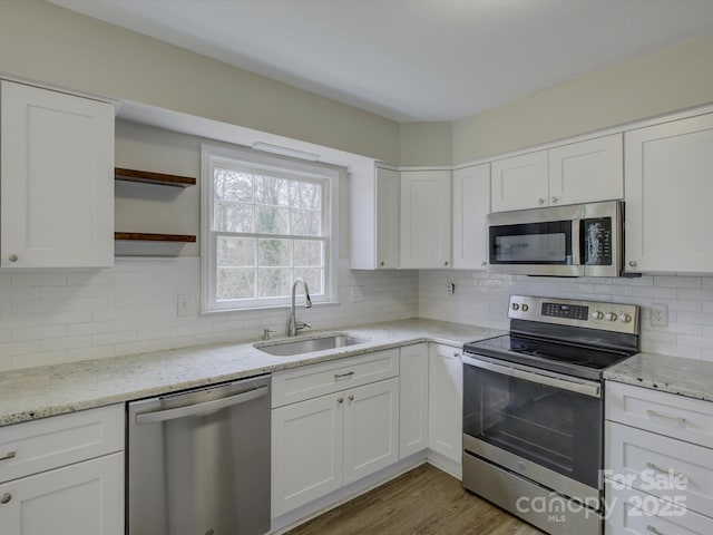 kitchen with wood finished floors, appliances with stainless steel finishes, a sink, and white cabinetry