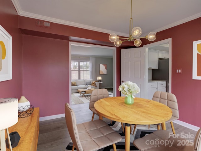 dining room featuring baseboards, visible vents, ornamental molding, and wood finished floors