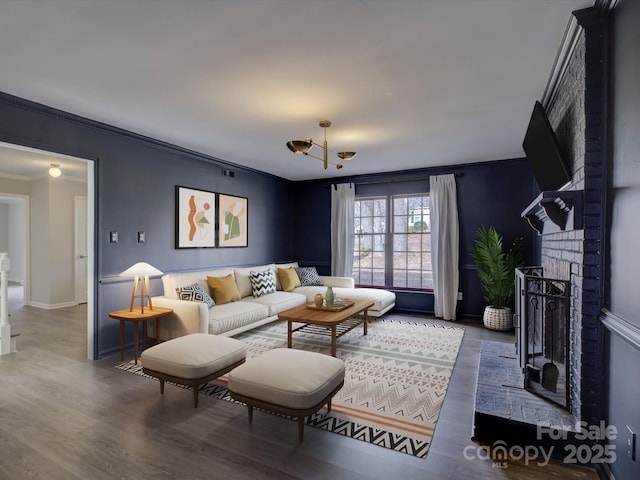 living room with a brick fireplace, crown molding, and wood finished floors