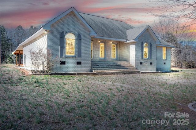 view of front of house with roof with shingles, a lawn, and brick siding