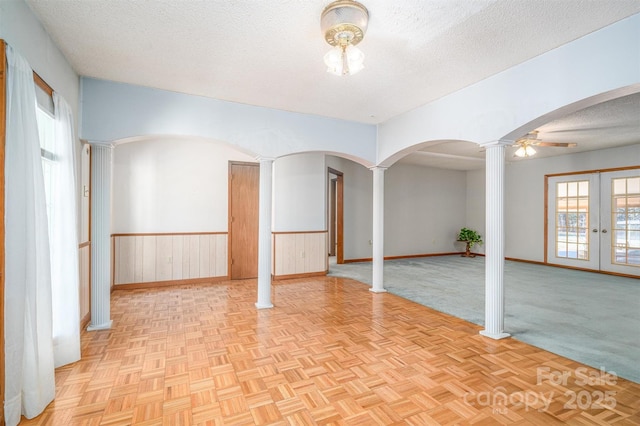 spare room featuring decorative columns, arched walkways, a wainscoted wall, a textured ceiling, and french doors