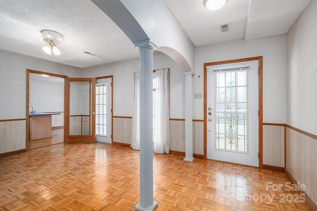 interior space featuring a wainscoted wall, decorative columns, wooden walls, and a textured ceiling