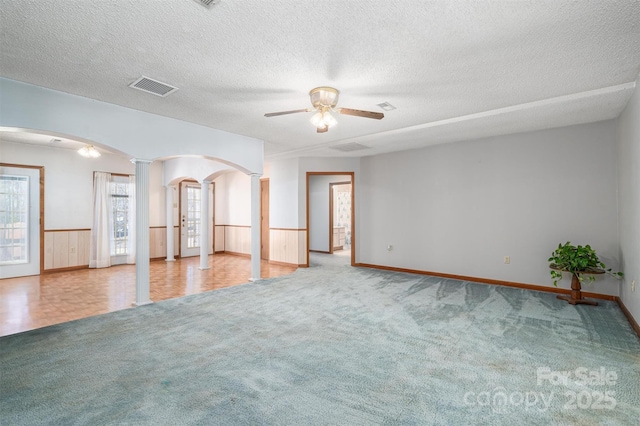 empty room featuring arched walkways, a wainscoted wall, decorative columns, visible vents, and light carpet