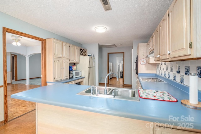 kitchen featuring white appliances, arched walkways, a sink, light countertops, and backsplash