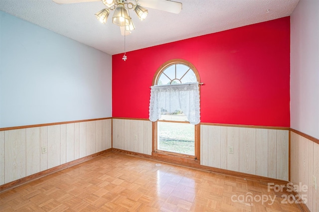 empty room with a wainscoted wall, ceiling fan, wood walls, and a textured ceiling