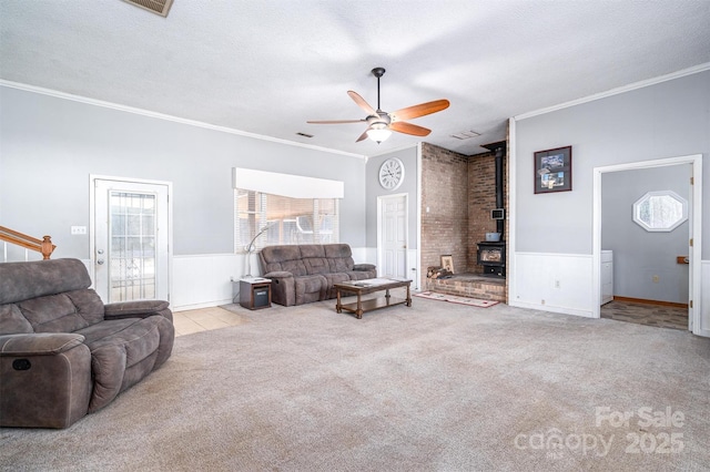 living area with a textured ceiling, light carpet, a ceiling fan, ornamental molding, and a wood stove