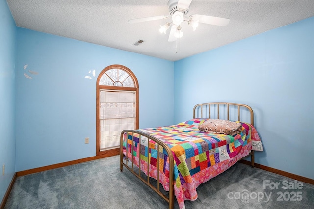 bedroom with a ceiling fan, visible vents, dark colored carpet, and a textured ceiling