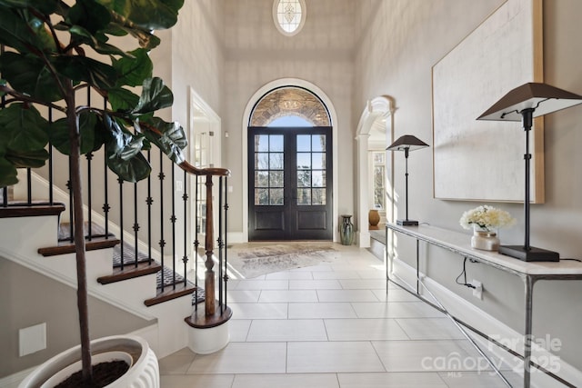 foyer entrance with french doors, stairway, a towering ceiling, and light tile patterned floors