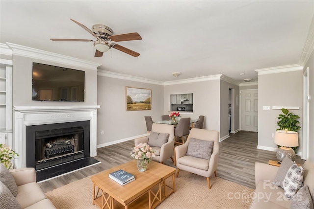 living area with a fireplace with raised hearth, ornamental molding, wood finished floors, and baseboards