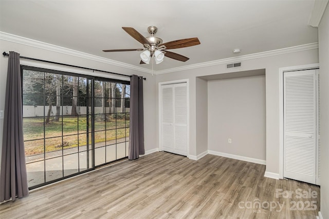 unfurnished bedroom featuring baseboards, light wood-style flooring, ornamental molding, and multiple closets