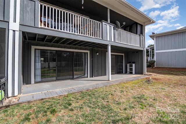 rear view of house with board and batten siding, a yard, and a patio