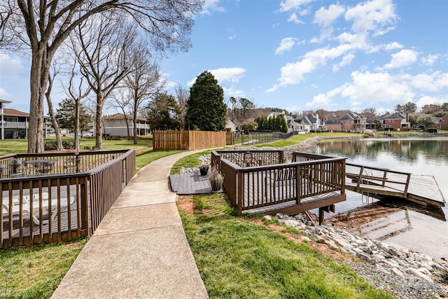 dock area featuring a lawn, a water view, fence, and a residential view