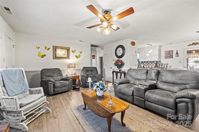 living room with a textured ceiling, ceiling fan, and light hardwood / wood-style flooring