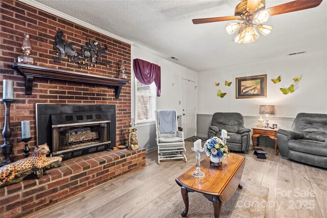 living room featuring a textured ceiling, ceiling fan, light wood-type flooring, and a brick fireplace