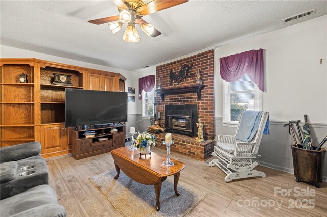 living room with a textured ceiling, a fireplace, a wealth of natural light, and light hardwood / wood-style flooring