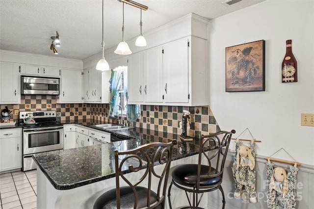 kitchen with stainless steel appliances, light tile patterned flooring, dark stone countertops, pendant lighting, and sink