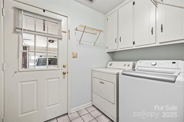 laundry area with a textured ceiling, washing machine and clothes dryer, light tile patterned floors, and cabinets