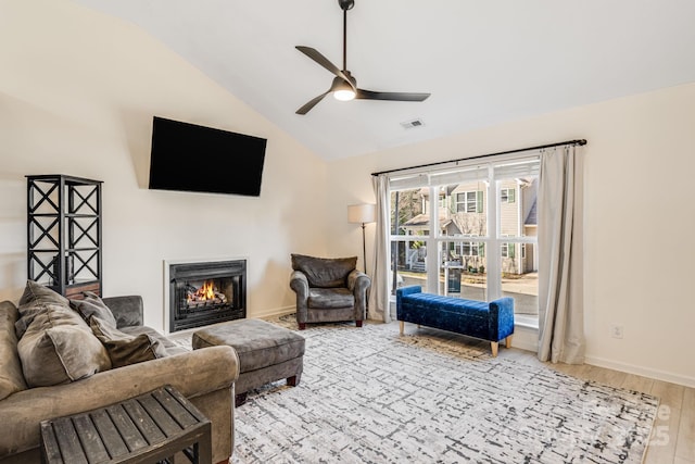 living area with lofted ceiling, a warm lit fireplace, wood finished floors, visible vents, and a ceiling fan