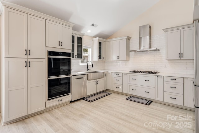 kitchen featuring dobule oven black, wall chimney exhaust hood, light countertops, gas stovetop, and stainless steel dishwasher