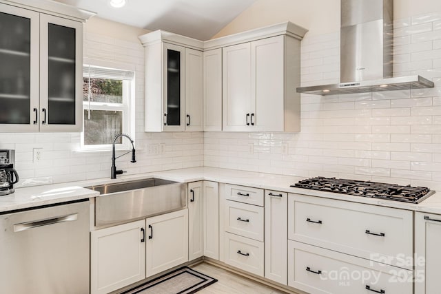 kitchen featuring tasteful backsplash, stainless steel dishwasher, a sink, wall chimney range hood, and black gas stovetop