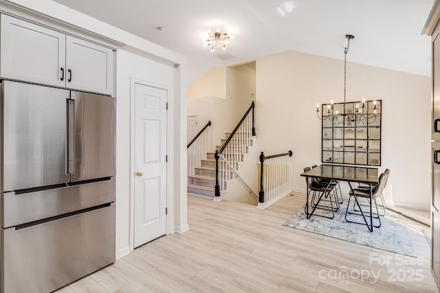 interior space featuring decorative light fixtures, light wood finished floors, lofted ceiling, an inviting chandelier, and high end refrigerator