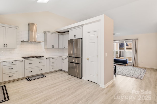 kitchen with vaulted ceiling, light countertops, wall chimney range hood, and freestanding refrigerator