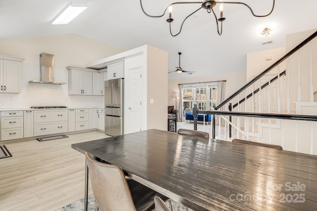 dining area with visible vents, stairs, vaulted ceiling, light wood-type flooring, and ceiling fan with notable chandelier