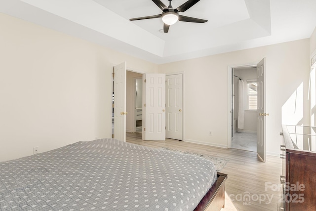 bedroom with a tray ceiling, wood finished floors, and baseboards