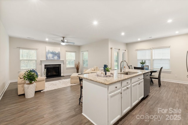 kitchen with a kitchen island with sink, a sink, white cabinetry, open floor plan, and stainless steel dishwasher